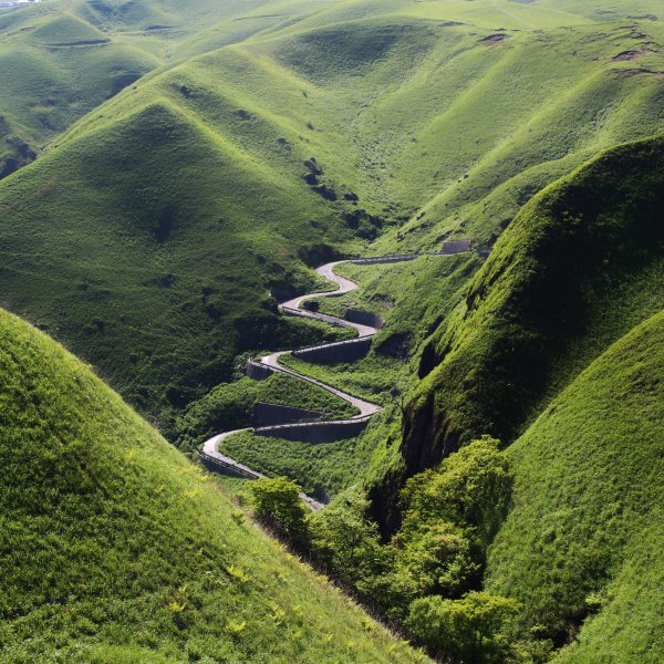 A zigzagging road surrounded by green mountains.