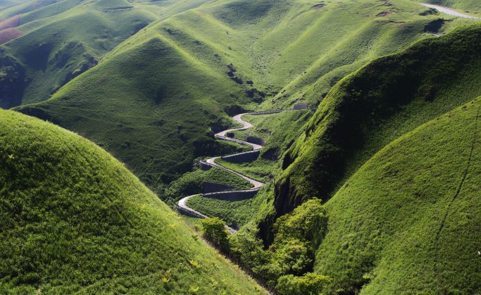 A zigzagging road surrounded by green mountains.